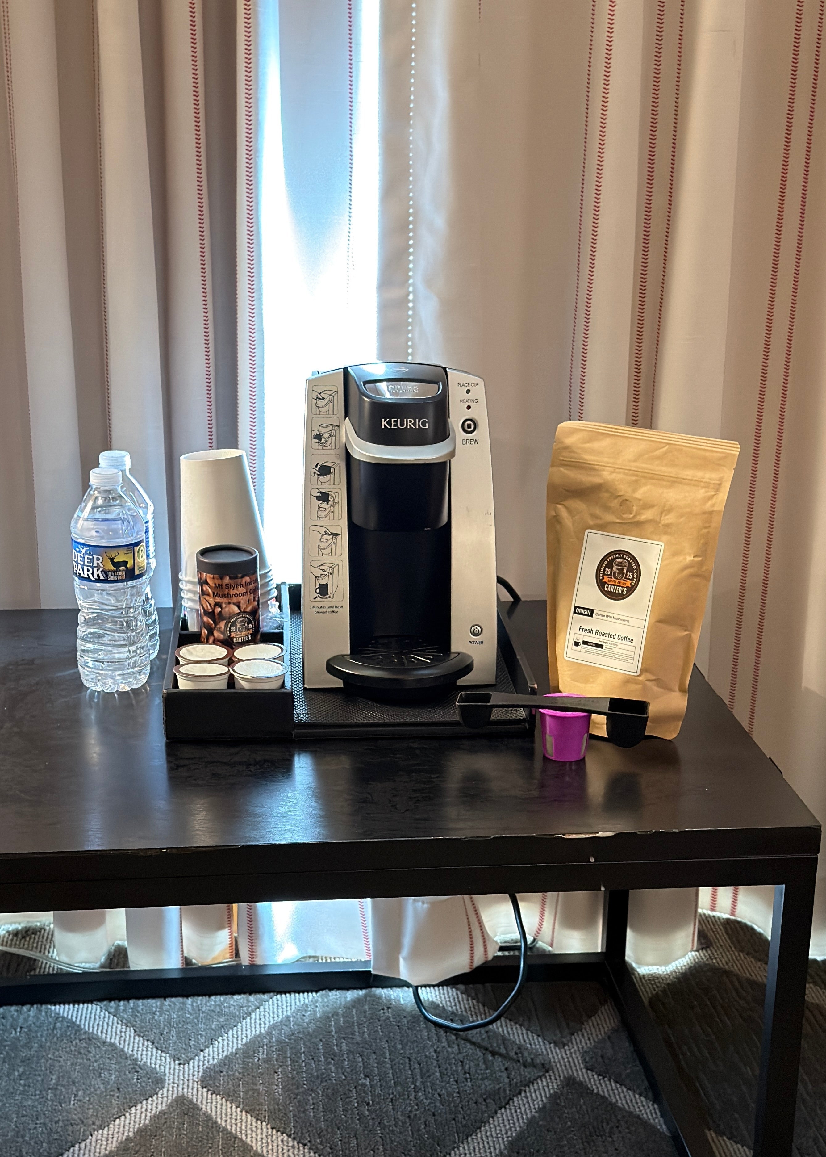 Coffee maker with a bag of coffee, water bottle, and other items on a table.